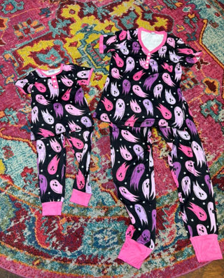 Two sets of ghost print pajamas in pink and purple on a colorful rug.