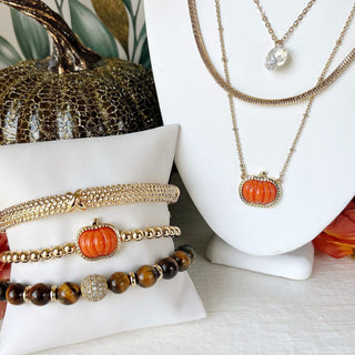 Gold-tone necklace with an orange pumpkin pendant displayed on a jewelry stand.