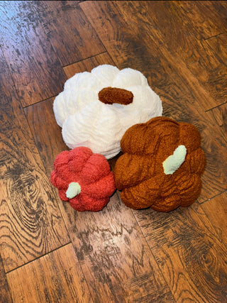 Three plush pumpkin pillows in white, orange, and red, displayed on a wooden floor.