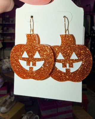 Orange glitter Jack O' Lantern earrings with white painted features on a display card.