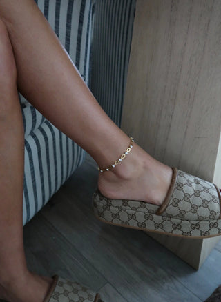 Gold anklet with circular links and pearl accents on a person's ankle.