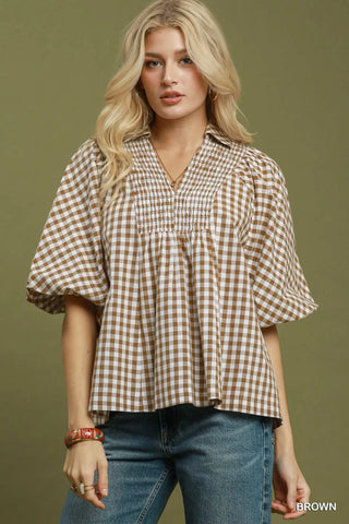 A brown gingham blouse with a smocked yoke and elbow-length puff sleeves.